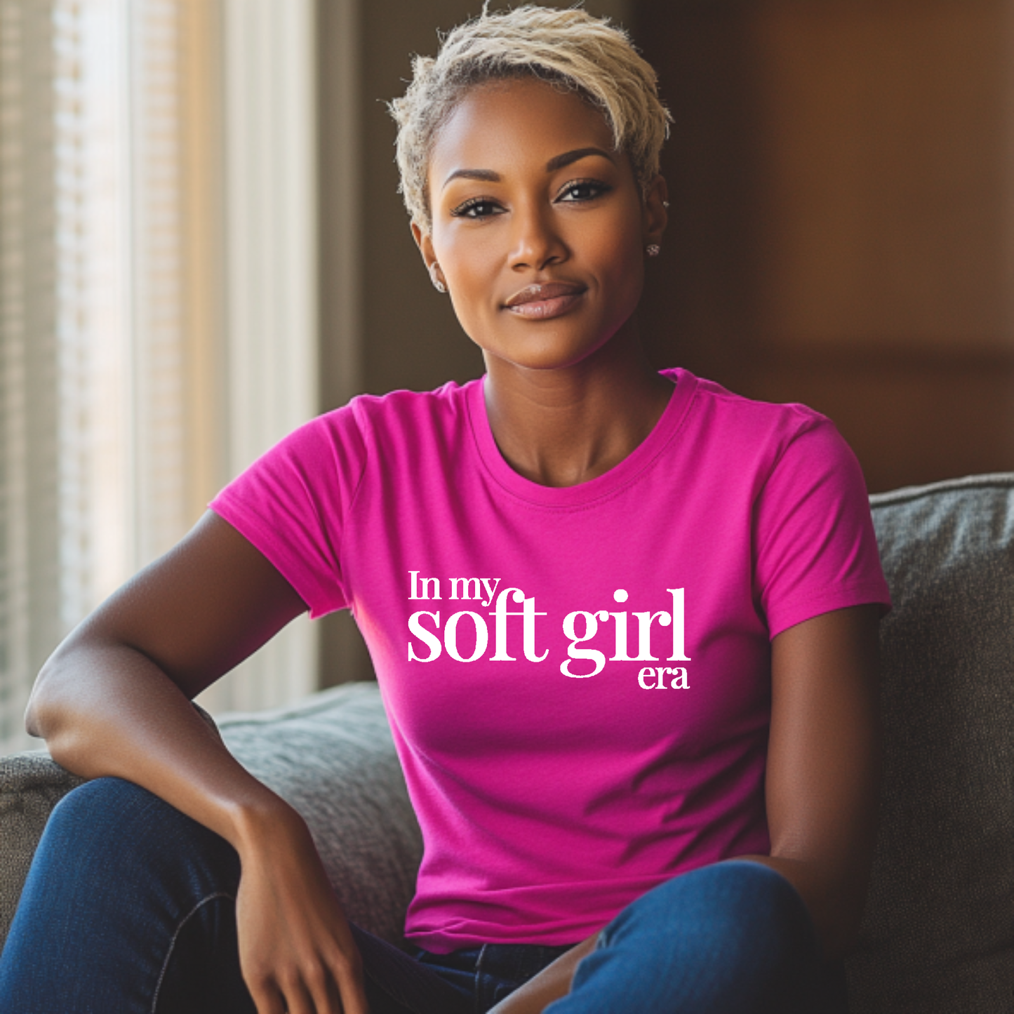 Woman wearing a pink t-shirt with text in my soft girl era sitting on a couch.
