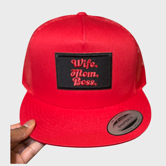 A red snapback hat with a black label that has 'Wife. Mom. Boss.' written in red.